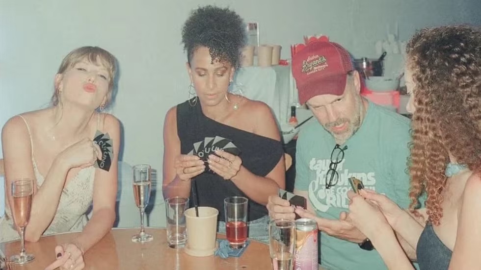 Taylor Swift and Jason Sudeikis seated at the UNO table with Spill It RTD Hibiscus and Friends in frame